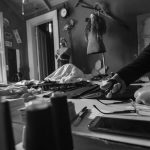 A black and white image capturing a seamstress working in a vintage workshop with tools.