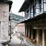 Picturesque street scene in a quaint Greek village featuring rustic stone houses and scenic mountain backdrop.